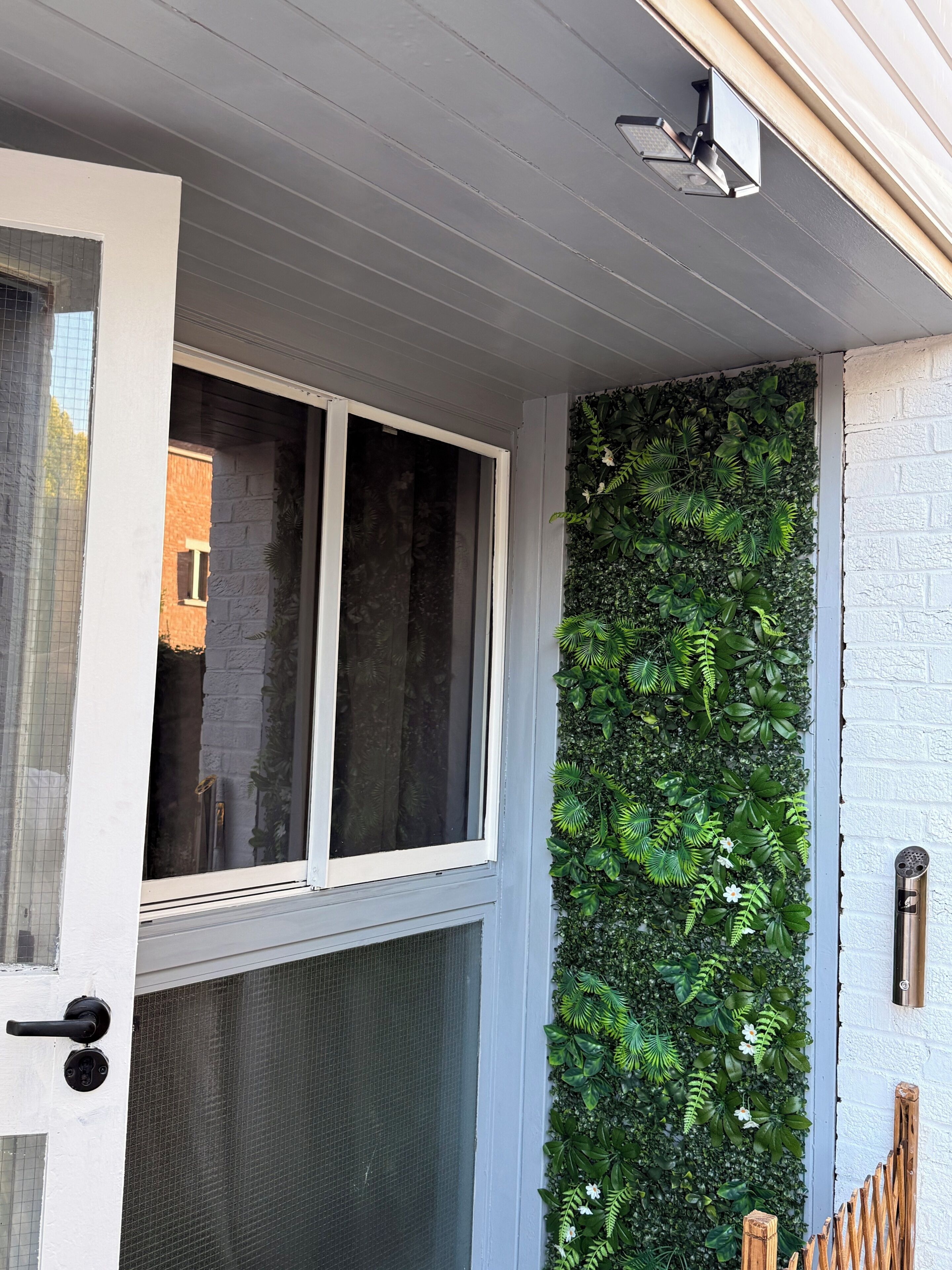 Un ingresso di un edificio con una porta bianca, una finestra e un muro ricoperto da vegetazione verde.
