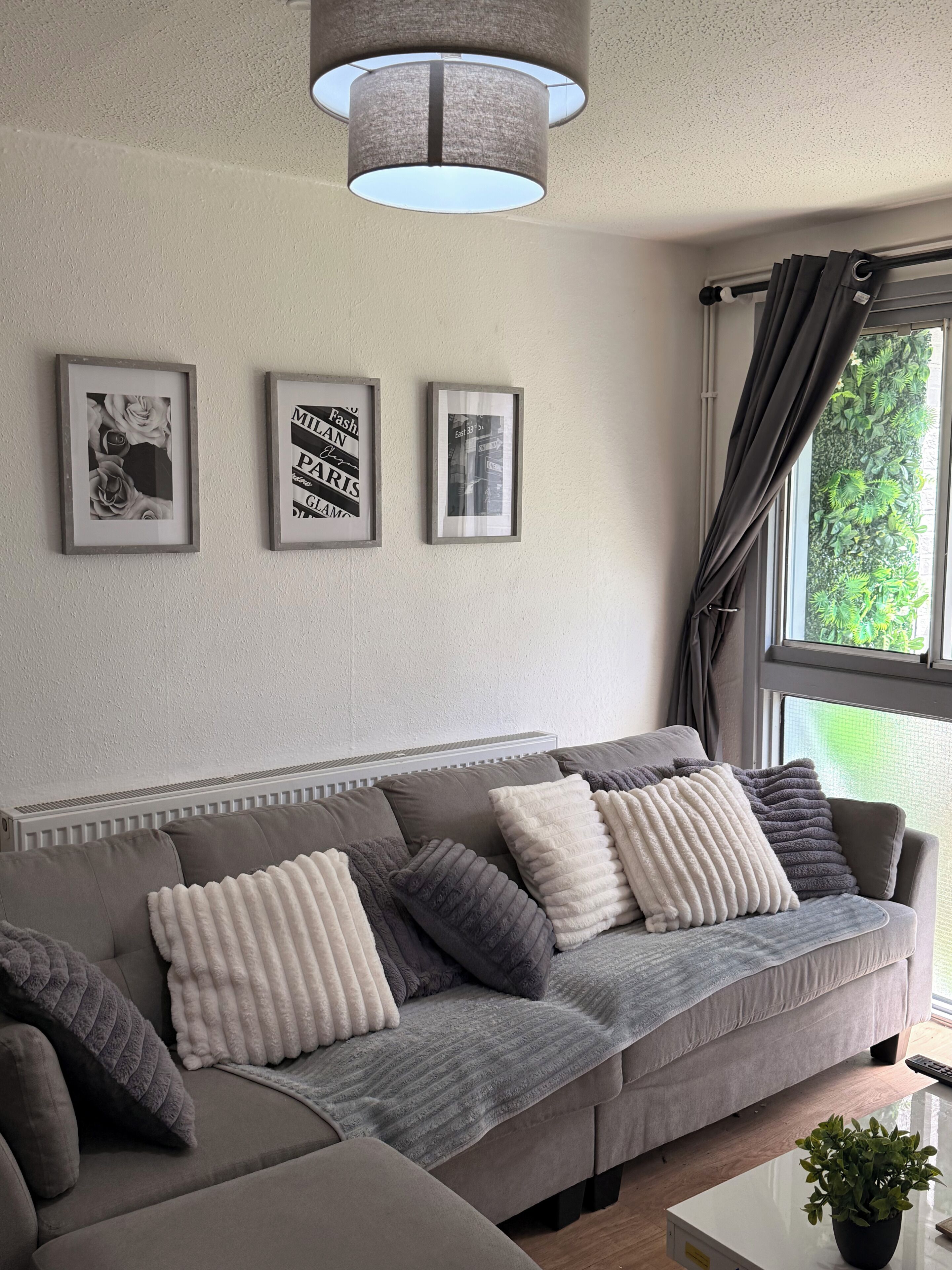 A modern living room with a grey sofa, decorative pillows, and framed artwork on the wall.