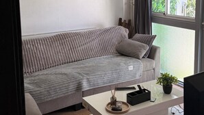 Un salon moderne avec un canapé gris, une table basse blanche agrémentée d’une plante, et des certificats encadrés accrochés au mur.