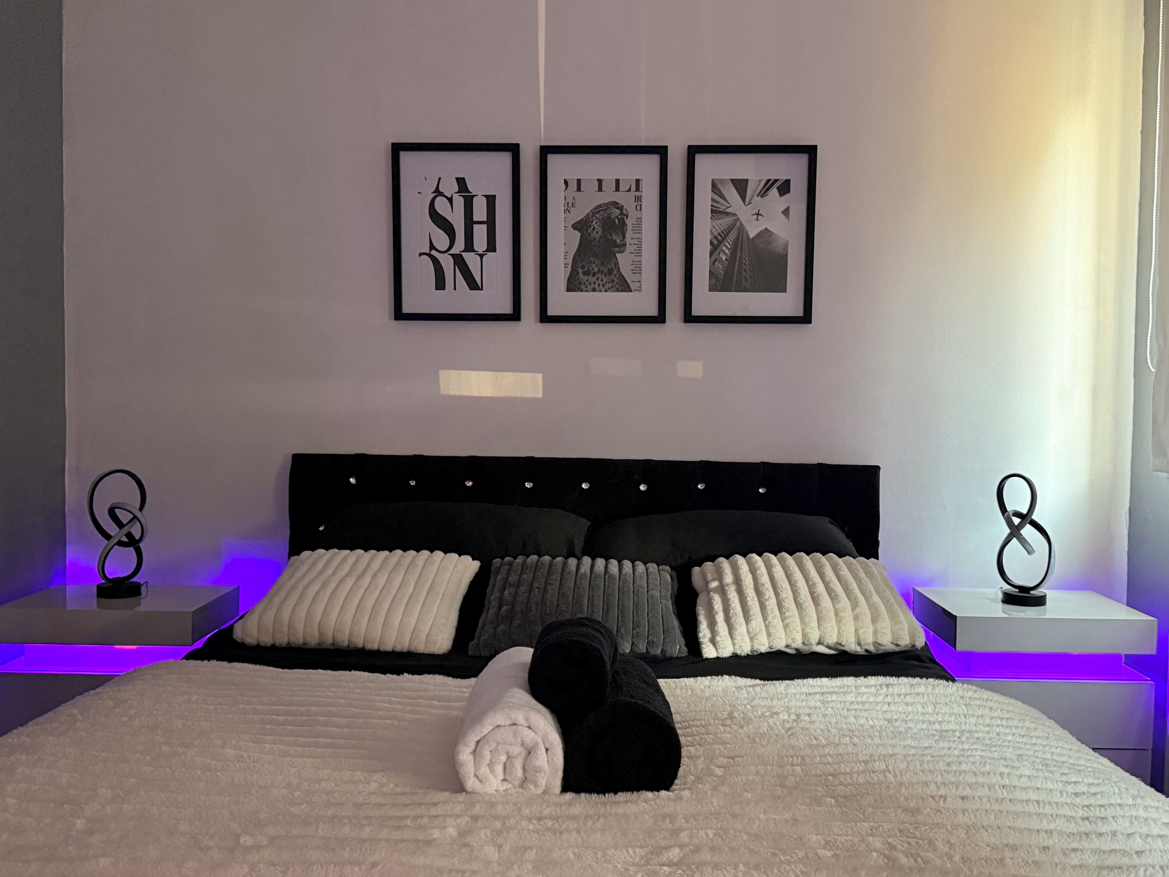 A neatly made bed with a black headboard, two bedside tables with decorative items, and three framed pictures on the wall.