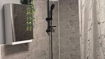 A bathroom with a white sink, a mirror, a shower with a black hose, and a curtain.
