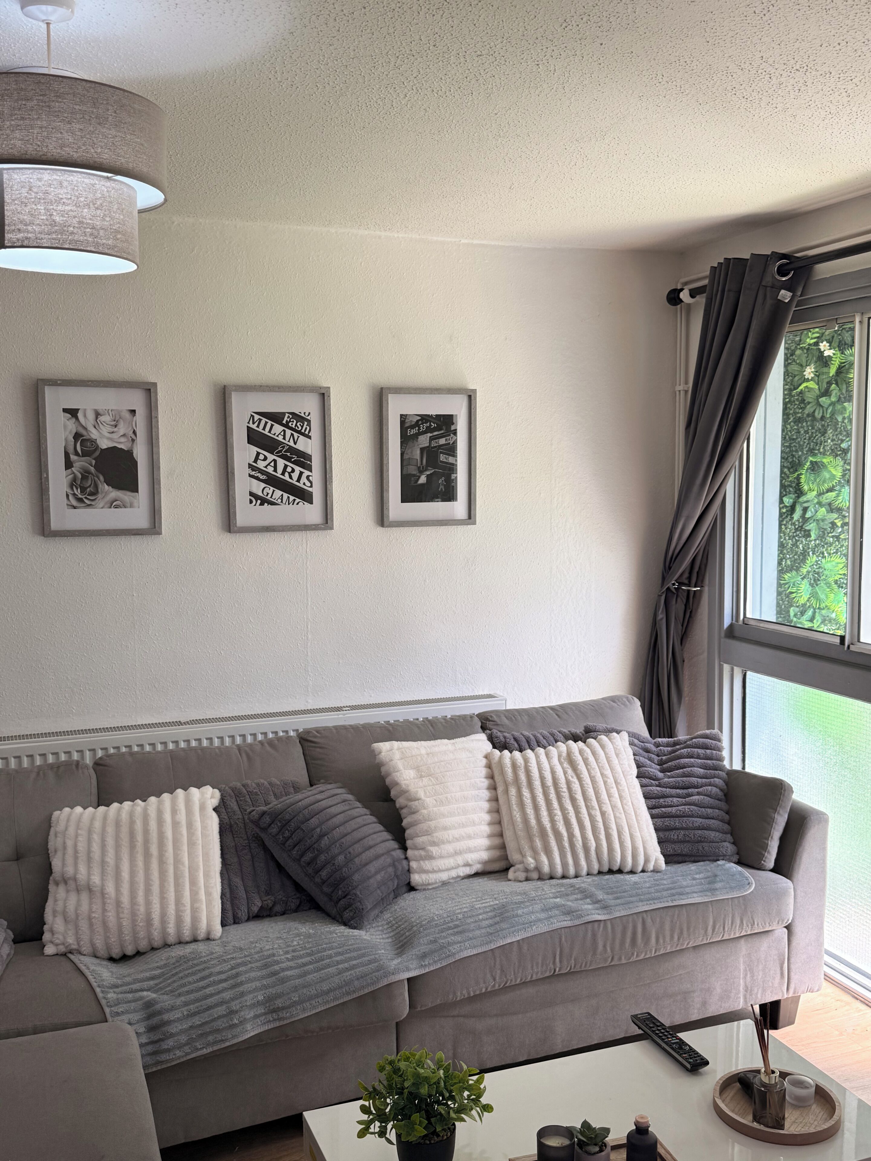 A modern living room with a grey sofa, framed pictures on the wall, and a window with curtains.