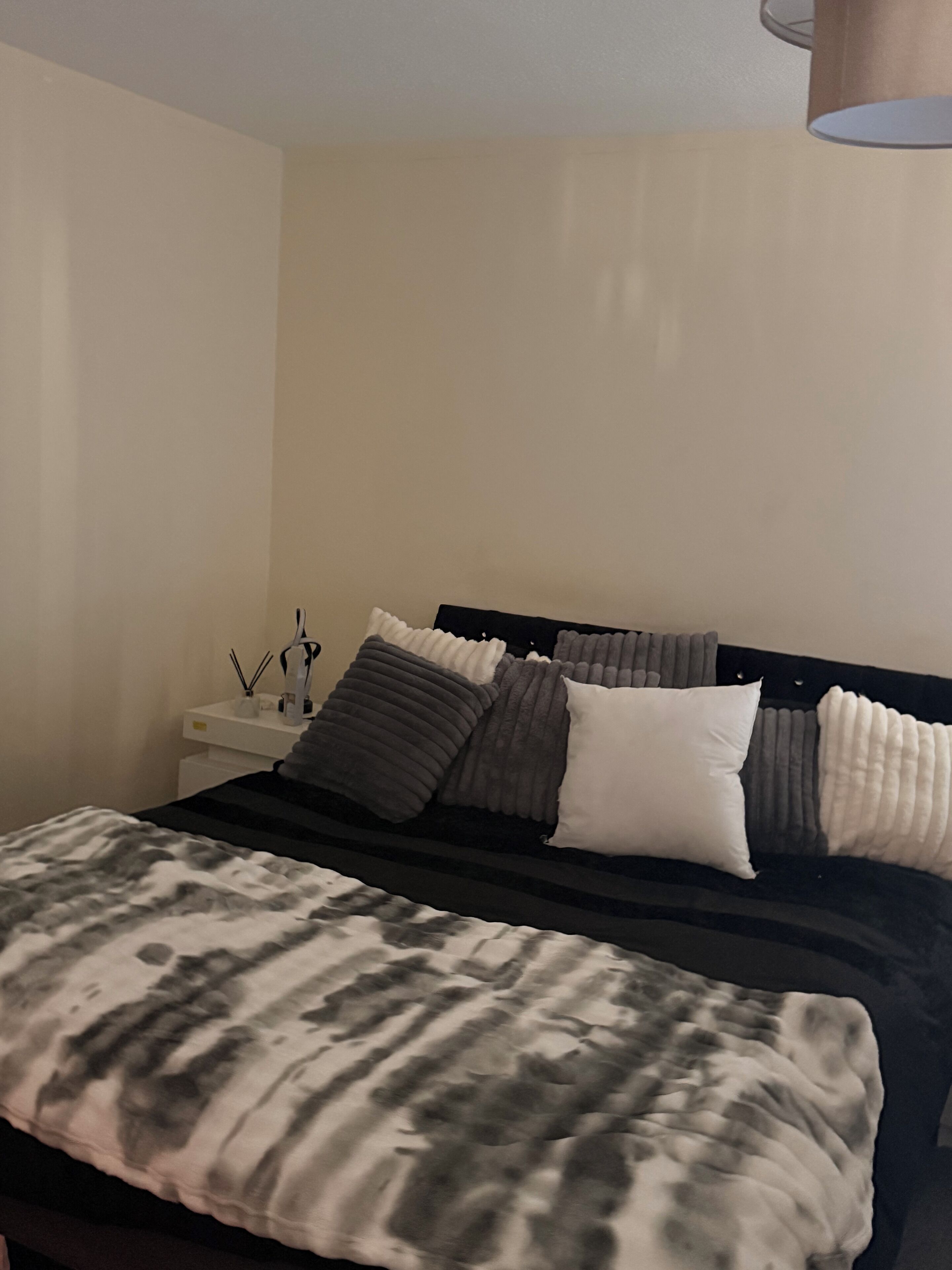A bedroom with a bed, pillows, a bedside table, and a lamp.