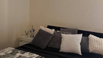 A bedroom with a bed, pillows, a bedside table, and a lamp.