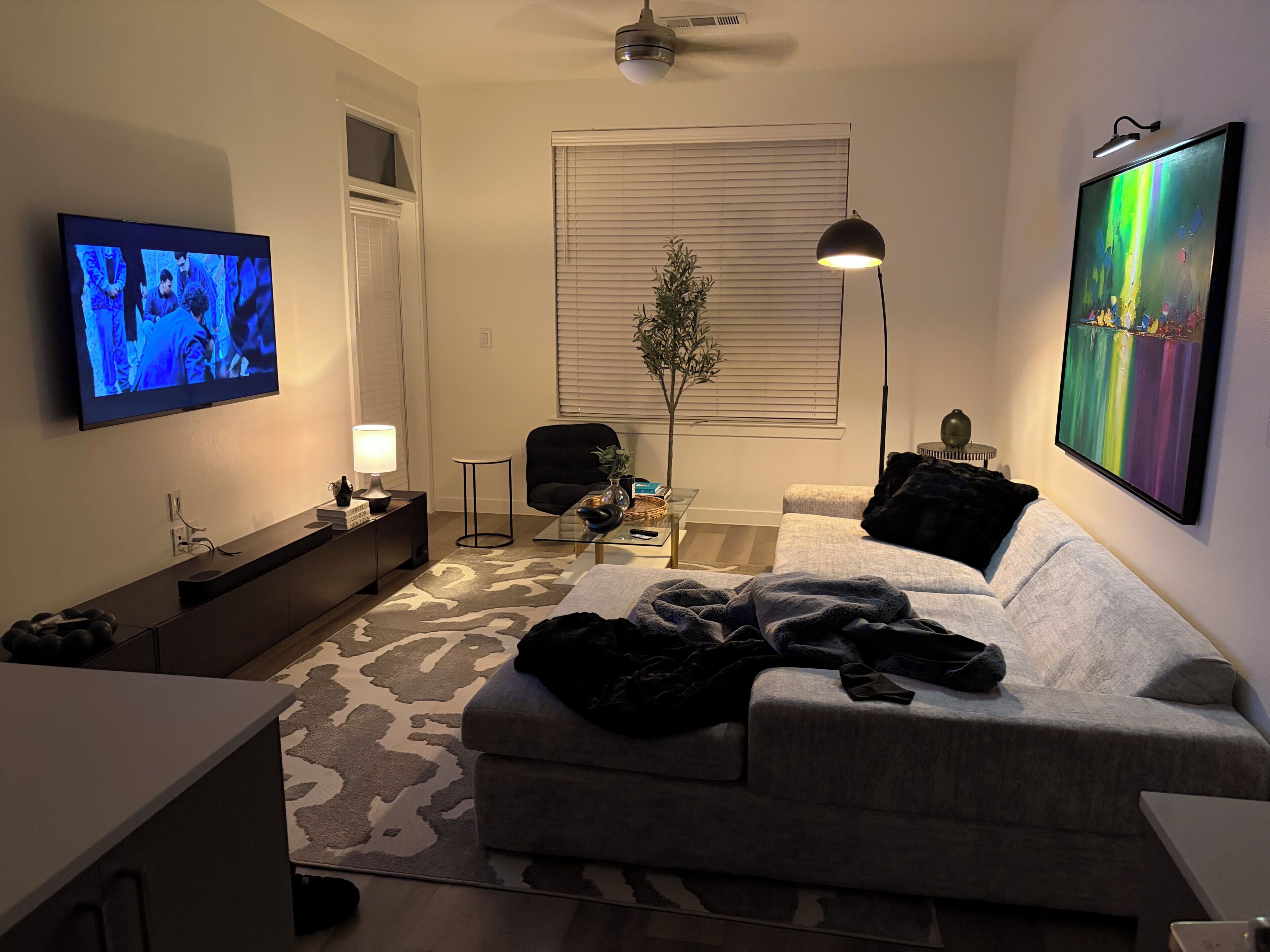 A living room with a flat-screen TV, a sofa, a coffee table, a lamp, and a painting on the wall.