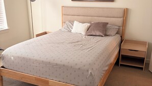 Een slaapkamer met een bed, nachtkastje, lamp en een schilderij aan de muur.