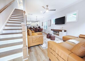 A modern living room with a staircase, leather sofas, a dining area, and a TV mounted on the wall. - 7 Min to Duke + Downtown | Free Parking (Durham)