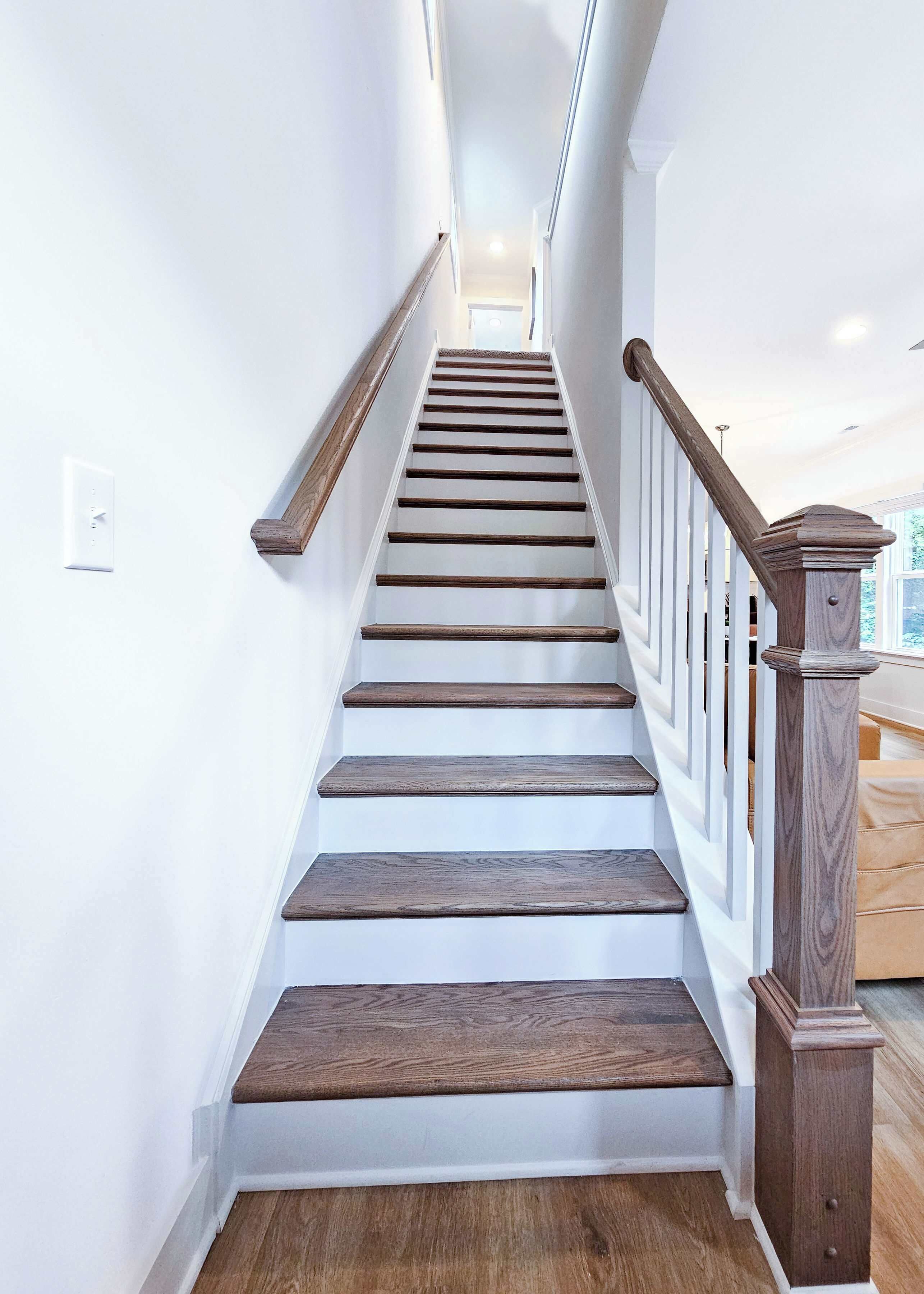 Un escalier avec des marches en bois et des murs blancs, menant à une pièce offrant une vue dégagée.