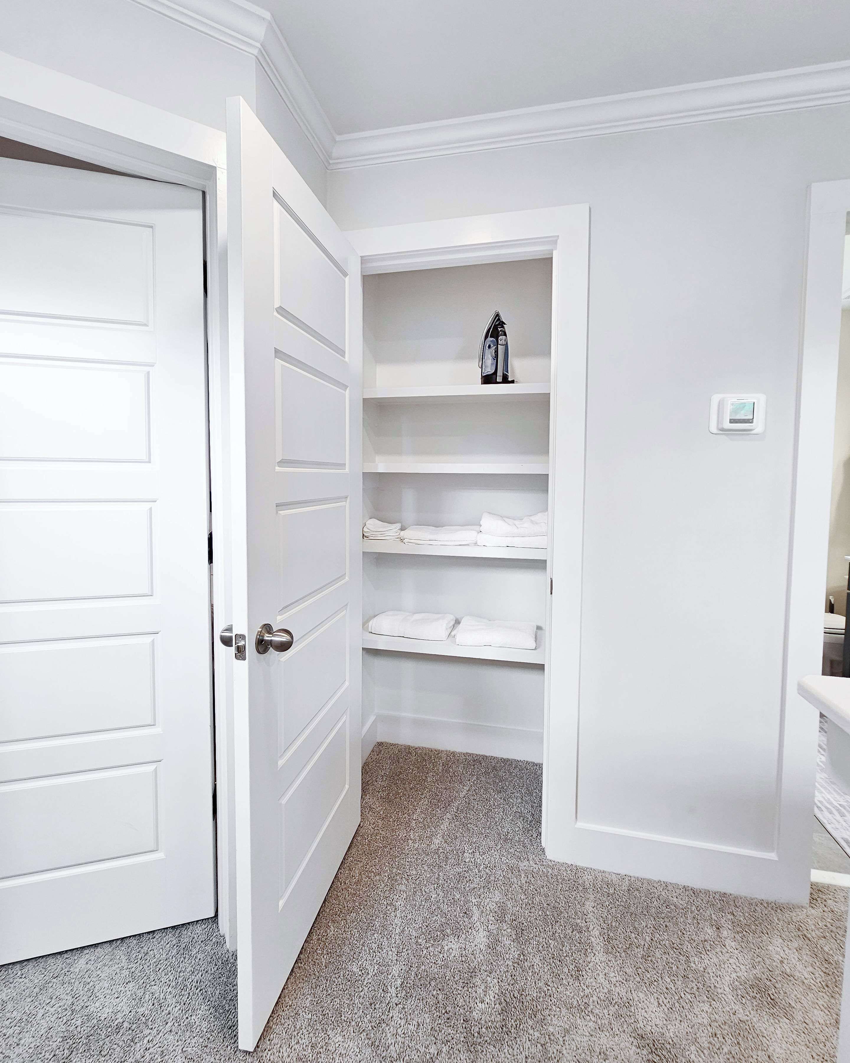 A white closet with shelves, a door, and a thermostat.