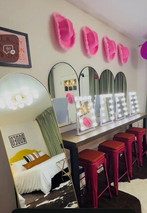 A room with a bed, a vanity with mirrors and lights, and pink slippers on the wall. - Pink GLAM Getaway Private on Wine Trail Pro Karaoke Cowboy Pool Firepit Hot Tub (Fredericksburg)