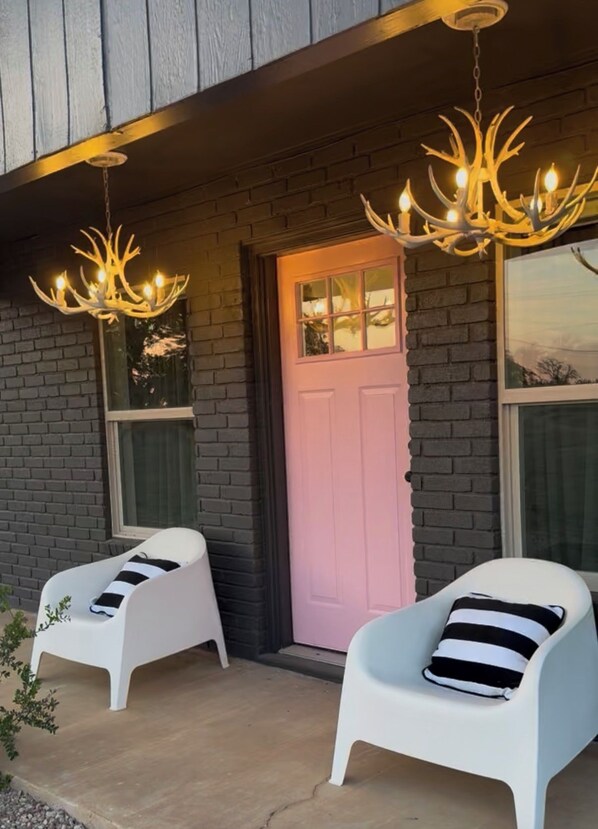 A building with a pink door, two white chairs with black and white striped cushions, and two chandeliers with light bulbs. - Pink GLAM Getaway Private on Wine Trail Pro Karaoke Cowboy Pool Firepit Hot Tub (Fredericksburg)