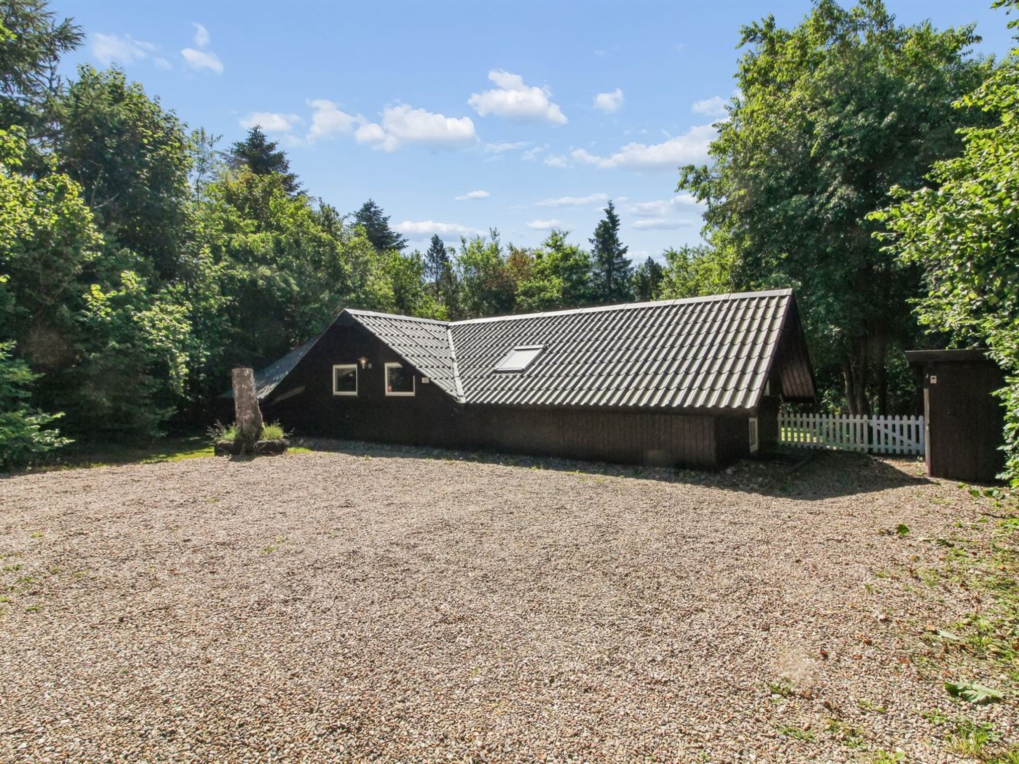 Un bâtiment d’un seul étage, doté d’un toit en pente, d’une allée en gravier et d’une zone délimitée par une clôture.