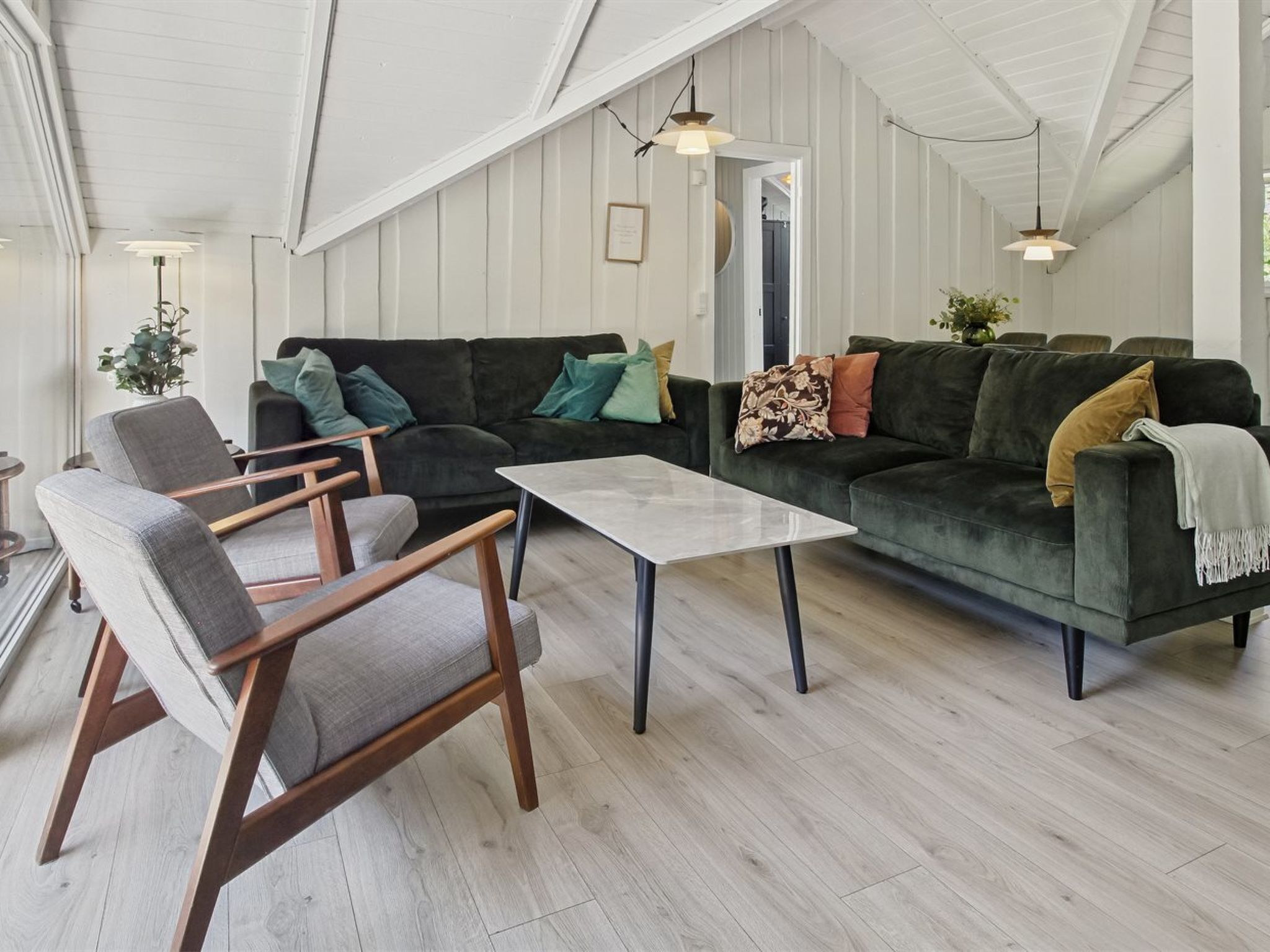 A spacious living room with a large dark green sofa, two armchairs, a coffee table, and wooden flooring.