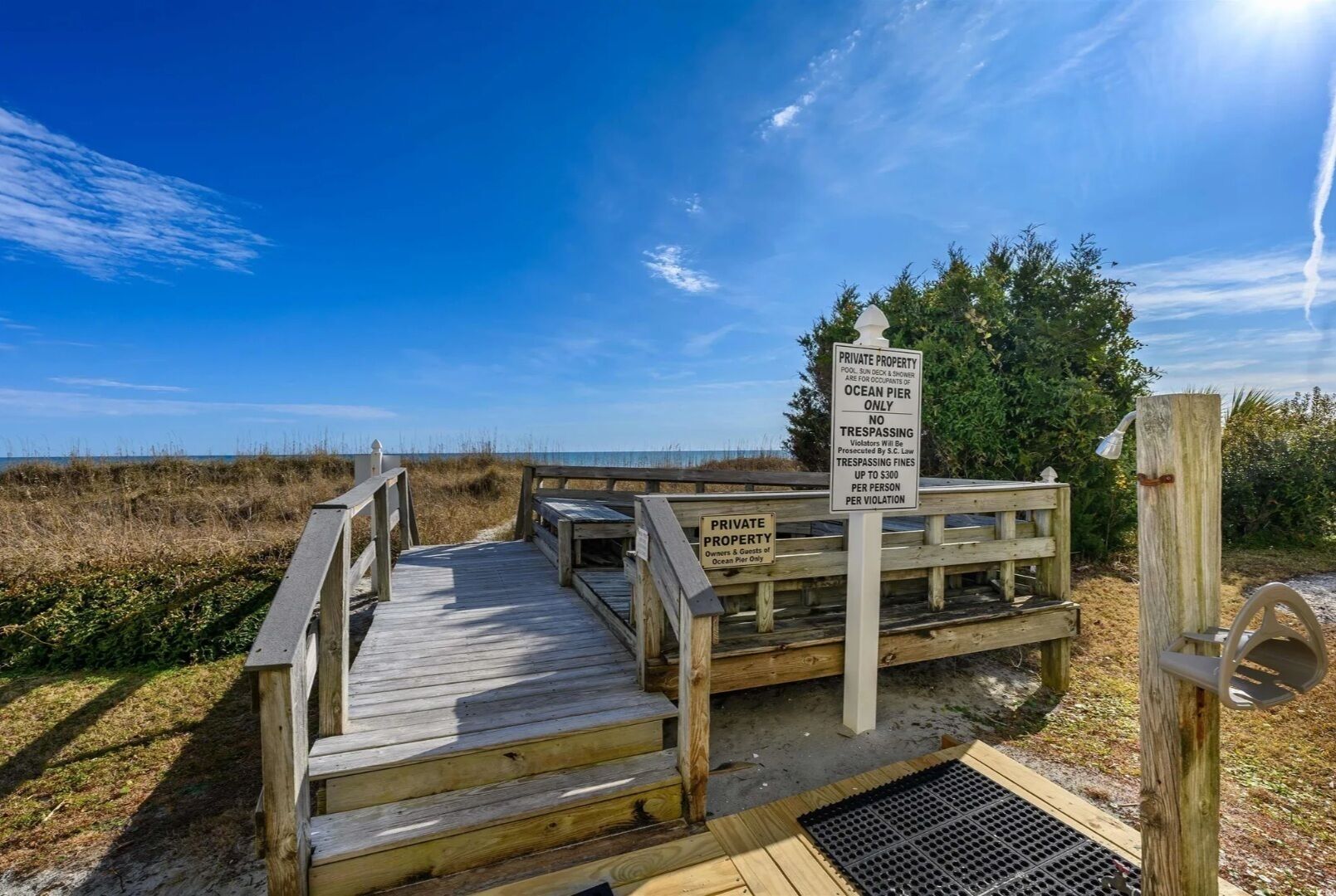 Ein Holzsteg führt zu einem privaten Strandabschnitt, mit einem Schild, das betritt Verbot und Privateigentum anzeigt.