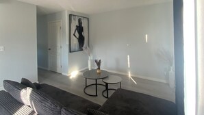 Een moderne woonkamer met een hoekbank, een klein rond salontafeltje en een schilderij aan de muur.