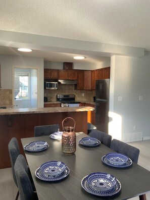 A modern kitchen with wooden cabinets, a central island, and a dining area with a table set for four. - Beautiful 3 bedroom Home in Calgary NE (Calgary)