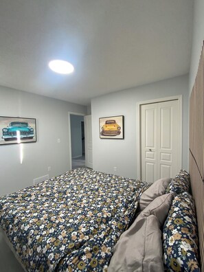 A bedroom with a bed, two wall-mounted pictures, a door, and a ceiling light. - Beautiful 3 bedroom Home in Calgary NE (Calgary)