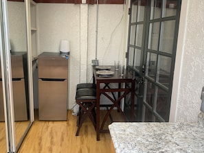 A compact kitchen with a refrigerator, a dining table with chairs, and a window with a view. - Spacious Studio Apartment 2 blocks to beach, town (Laguna Beach)