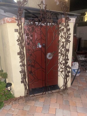 A metal gate with a star design, a red door, and a brick wall.