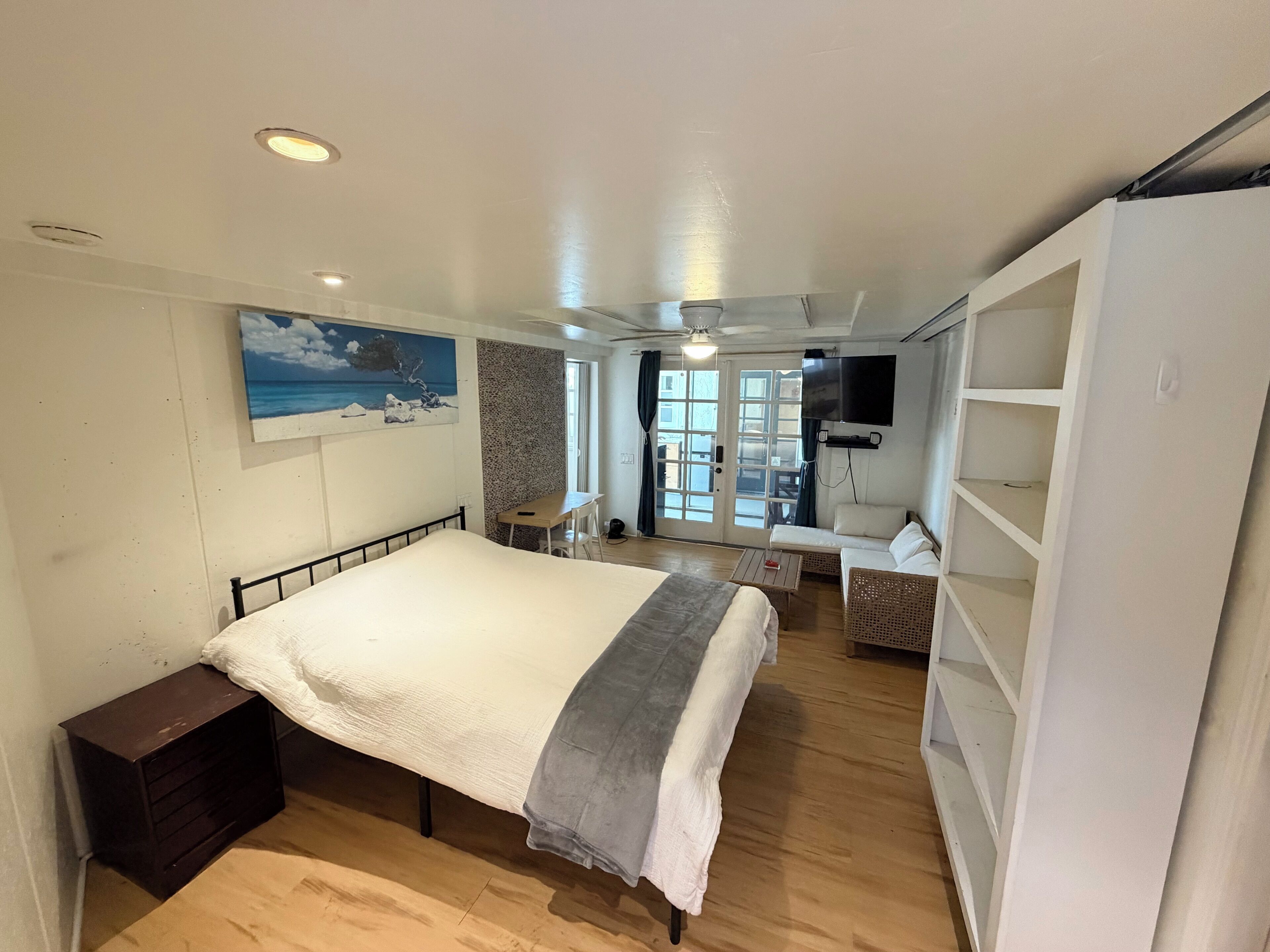 A bedroom with a bed, a desk, a TV, and a view of the outside.