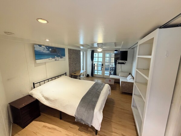 A bedroom with a bed, a desk, a TV, and a view of the outside.