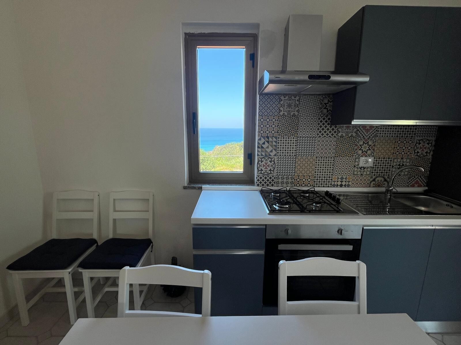 Eine kleine Küche mit Gasherd, einem Fenster mit Meerblick und einer backsplash mit Muster.