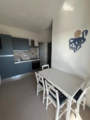 A modern kitchen with grey cabinets, a tiled backsplash, and a white dining table with chairs.