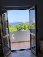 Una habitación con puerta de vidrio corrediza que da a un balcón con vistas al océano y follaje.