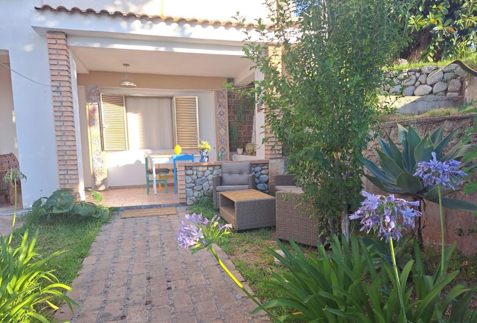 Un'area patio con mobili da esterno, un muro in pietra e diverse piante.