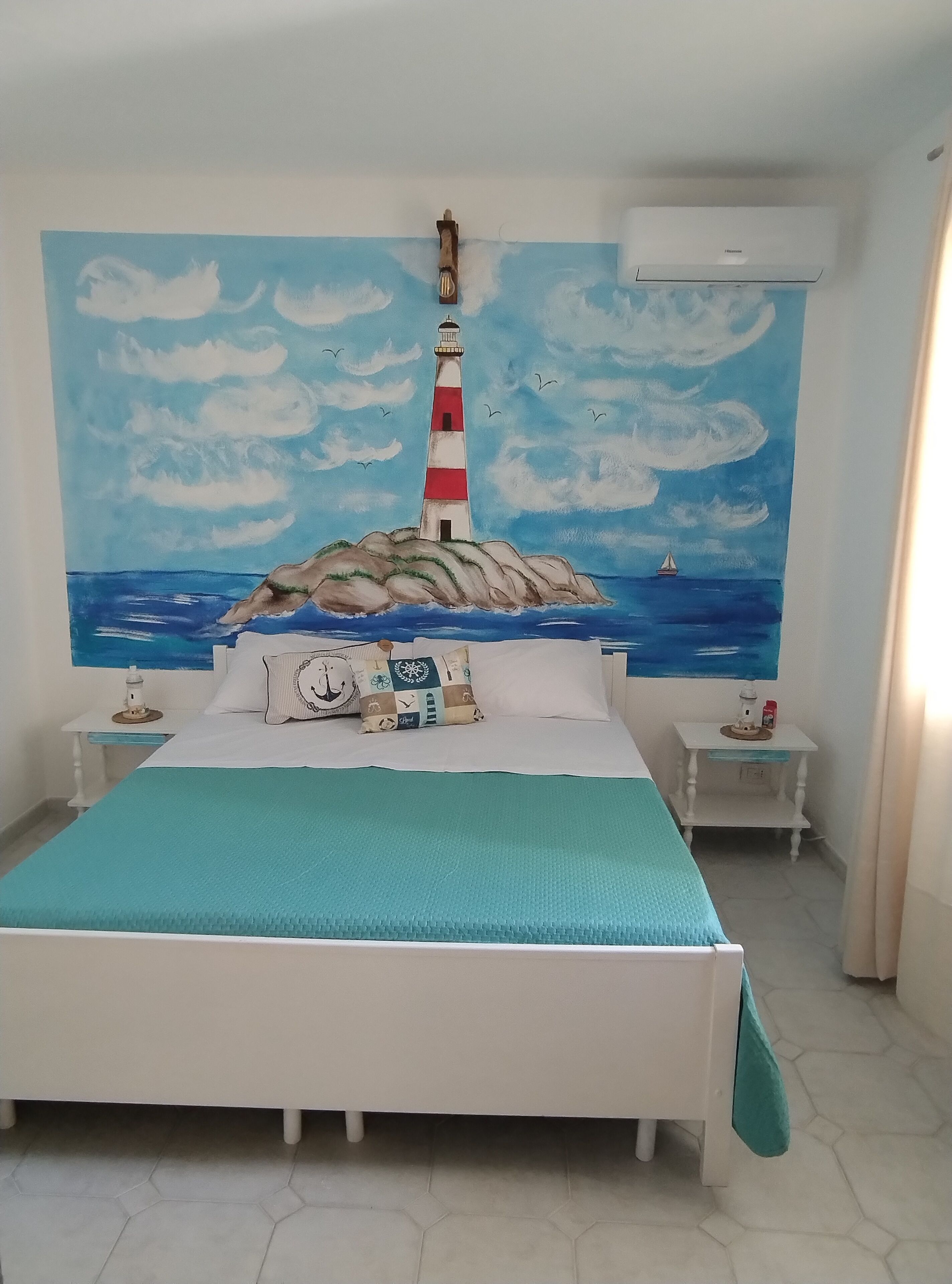 Una camera da letto con un letto, un comodino, un tavolino, un quadro raffigurante un faro e un condizionatore d'aria.