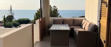A balcony with a view of the sea, a wicker table, and a sofa.