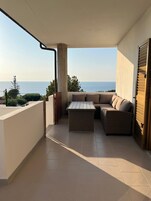 Un balcón con vista al mar, una mesa de mimbre y un sofá.