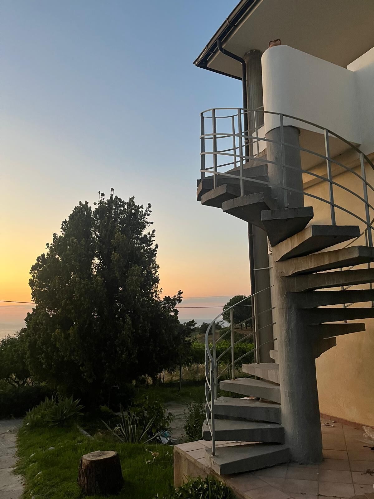 Una escalera de caracol conduce a un balcón con vistas a la puesta de sol y un árbol grande.
