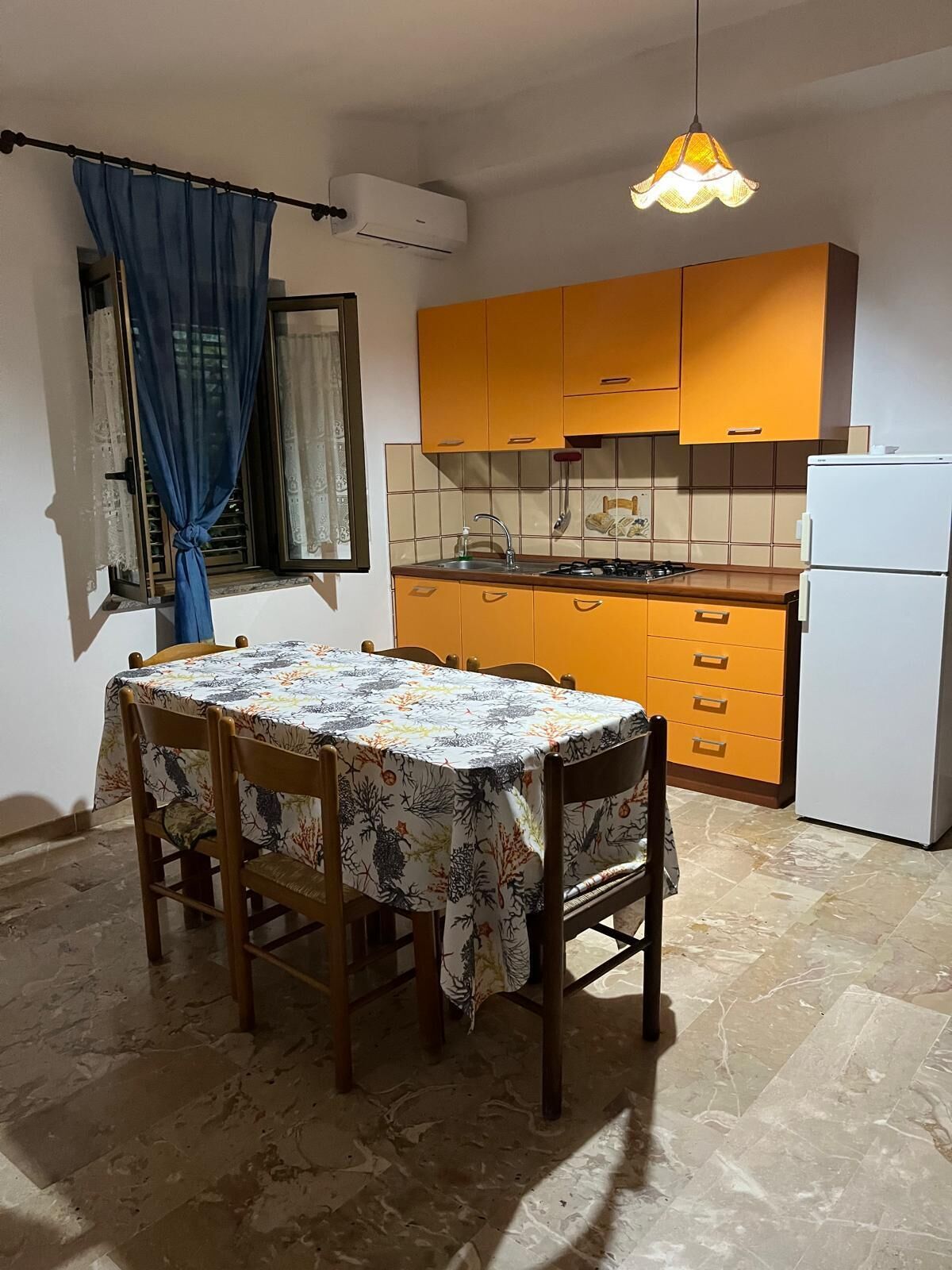 Una cucina funzionale con un tavolo da pranzo, sedie, un frigorifero e una lampada a sospensione.