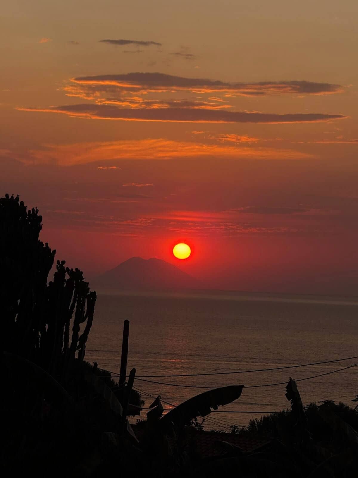 A sunset over a body of water with a silhouette of a mountain in the background.