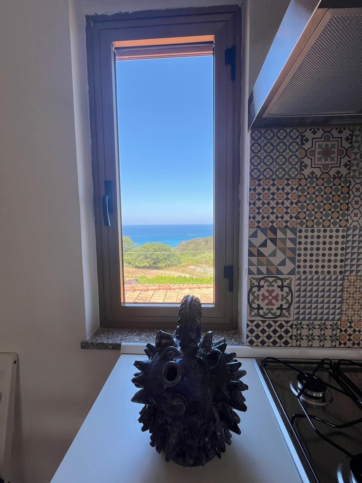 Eine Küche mit Fenster und Blick auf eine Landschaft, eine Dekoration auf der Arbeitsplatte und Wandfliesen mit Muster.