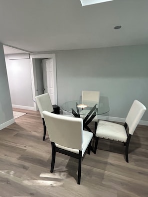 Un coin repas avec une table en verre et quatre chaises, une porte blanche et un plancher en bois.