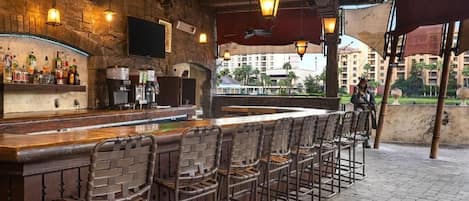 A bar area with a long counter, wicker chairs, and hanging lanterns.
