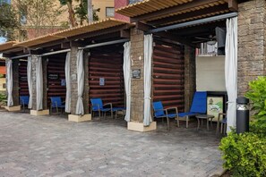 A covered outdoor seating area with chairs and tables, stone pillars, and a trash can. - Family 2BR Suite Balcony, Washer/Dryer & Wi-Fi (Lake Buena Vista)