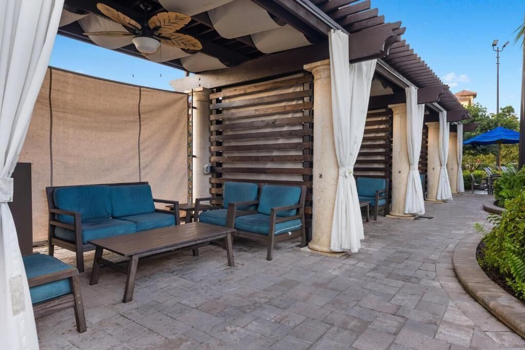 Ein möblierter Außenbereich mit Holzmöbeln, darunter Sofas und ein Tisch, sowie eine Pergola mit weißen Vorhängen.