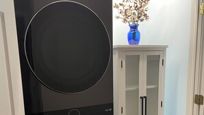 Eine moderne Küche mit schwarzen Geräten, einem weißen Schrank mit Glastüren und einer blauen Vase mit Trockenblumen.