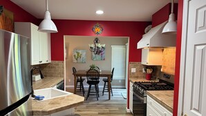 A kitchen with a dining area, stainless steel appliances, and a red accent wall. - 2BR Charlevoix Getaway - Walk to Lake Michigan Beach - Dog Friendly (Charlevoix)