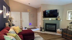 A living room with a sectional sofa, fireplace, television, and a door with a sign. - 2BR Charlevoix Getaway - Walk to Lake Michigan Beach - Dog Friendly (Charlevoix)