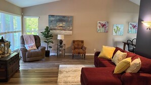 Ein Wohnzimmer mit einem roten Sofa, zwei Sesseln, einem Couchtisch und einem Gemälde an der Wand.