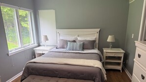 Ein Schlafzimmer mit einem großen Bett, einem Nachttisch, einer Kommode und einem Fenster mit Jalousien.