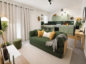 Un salón con un sofá verde, una mesita y una cocina al fondo.