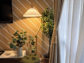 Una habitación con una lámpara, una planta en maceta, un televisor montado en la pared y una cortina.
