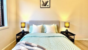 A bedroom with a bed, two bedside tables, a framed picture on the wall, and a window. - Bright Kalkallo Home, Easy Melbourne Access (Kalkallo)