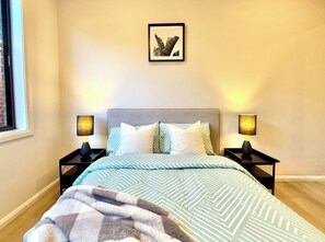 Ein Schlafzimmer mit einem Bett, zwei Nachttischen, einem gerahmten Bild an der Wand und einem Fenster.