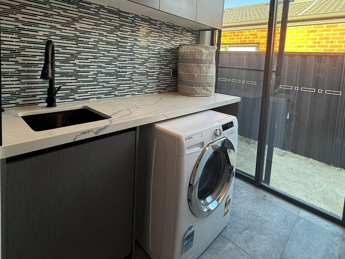 A compact kitchen with a built-in washing machine, a sink, and a tiled backsplash.
